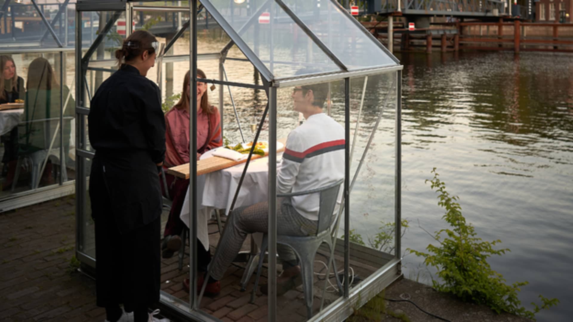 A server at Mediatic ETEN uses a wooden board to serve food to diners inside a greenhouse.