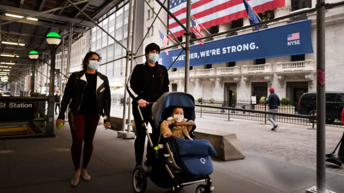 A family wearing masks passes the New York Stock Exchange, Tuesday, May 26, 2020.