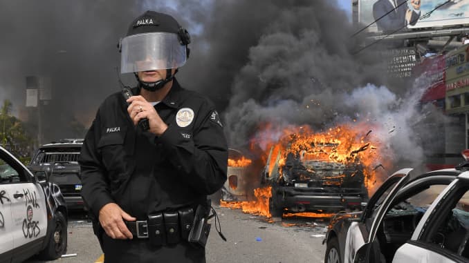 El comandante del Departamento de Policía de Los Ángeles, Cory Palka, se encuentra entre varios coches de policía destruidos mientras uno explota mientras arde durante una protesta por la muerte de George Floyd, el sábado 30 de mayo de 2020, en Los Ángeles.