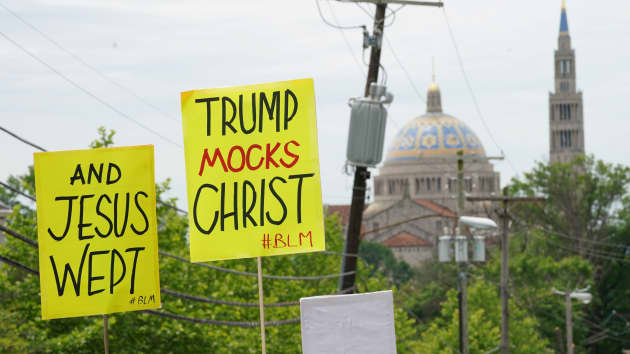 Protestors hold up signs as President Donald Trump's motorcade passes the Basilica of the National Shrine of the Immaculate Conception (at rear) and Catholic University on the way to the nearby Saint John Paul II National Shrine while protests continue ag