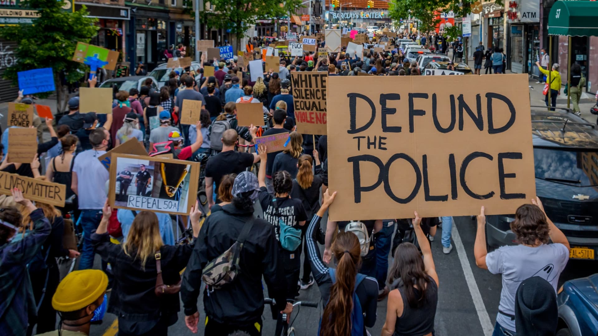 A participant holding a Defund The Police sign at the protest. Thousands of protesters filled the streets of Brooklyn in a massive march to demand justice for George Floyd, killed by Officer Derek Chauvin and to make a loud call for the defunding of the police force.