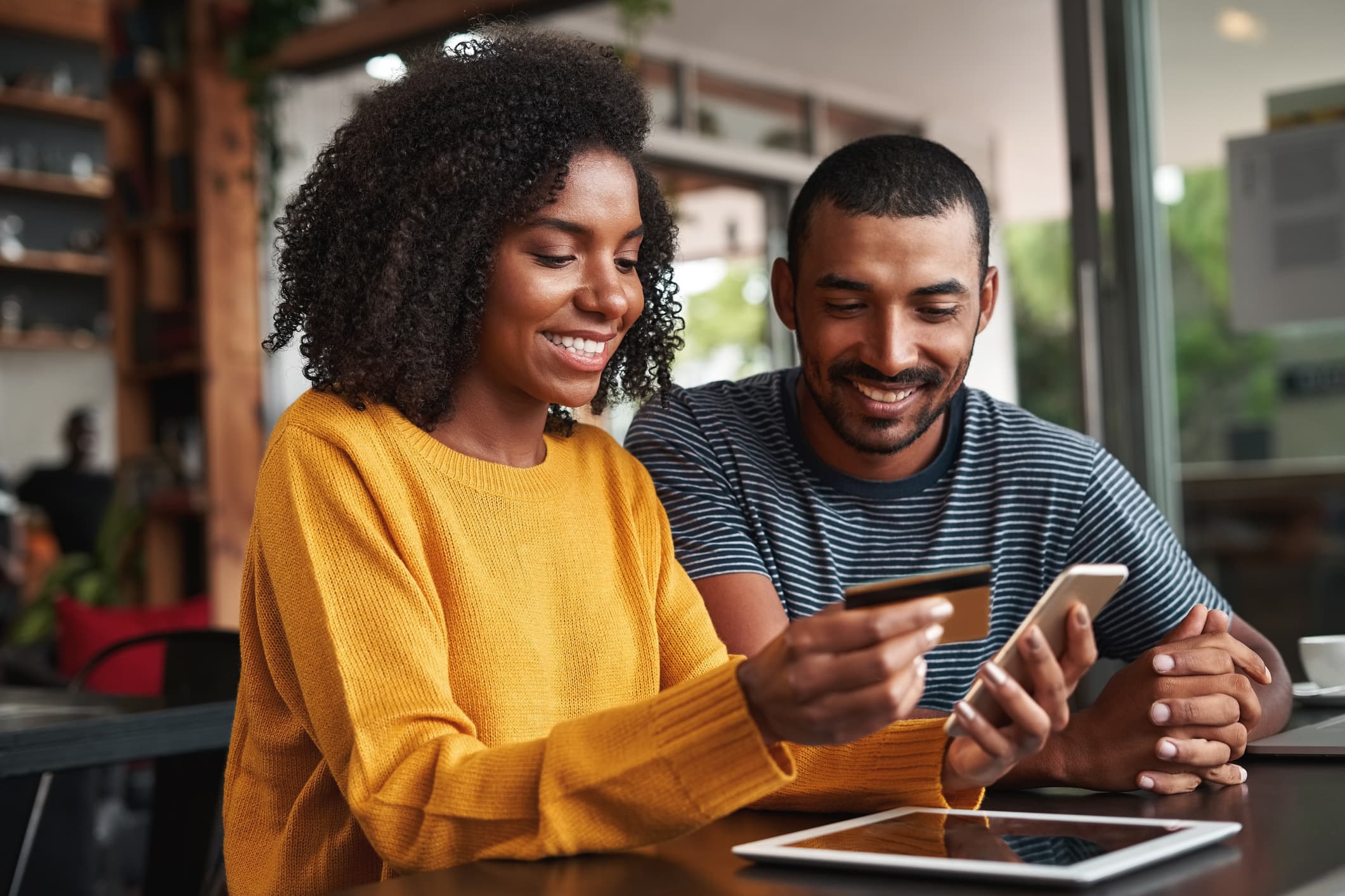 Молодой человек смотрит на свою девушку с помощью кредитной карты и смартфон для онлайн-покупок в кафе