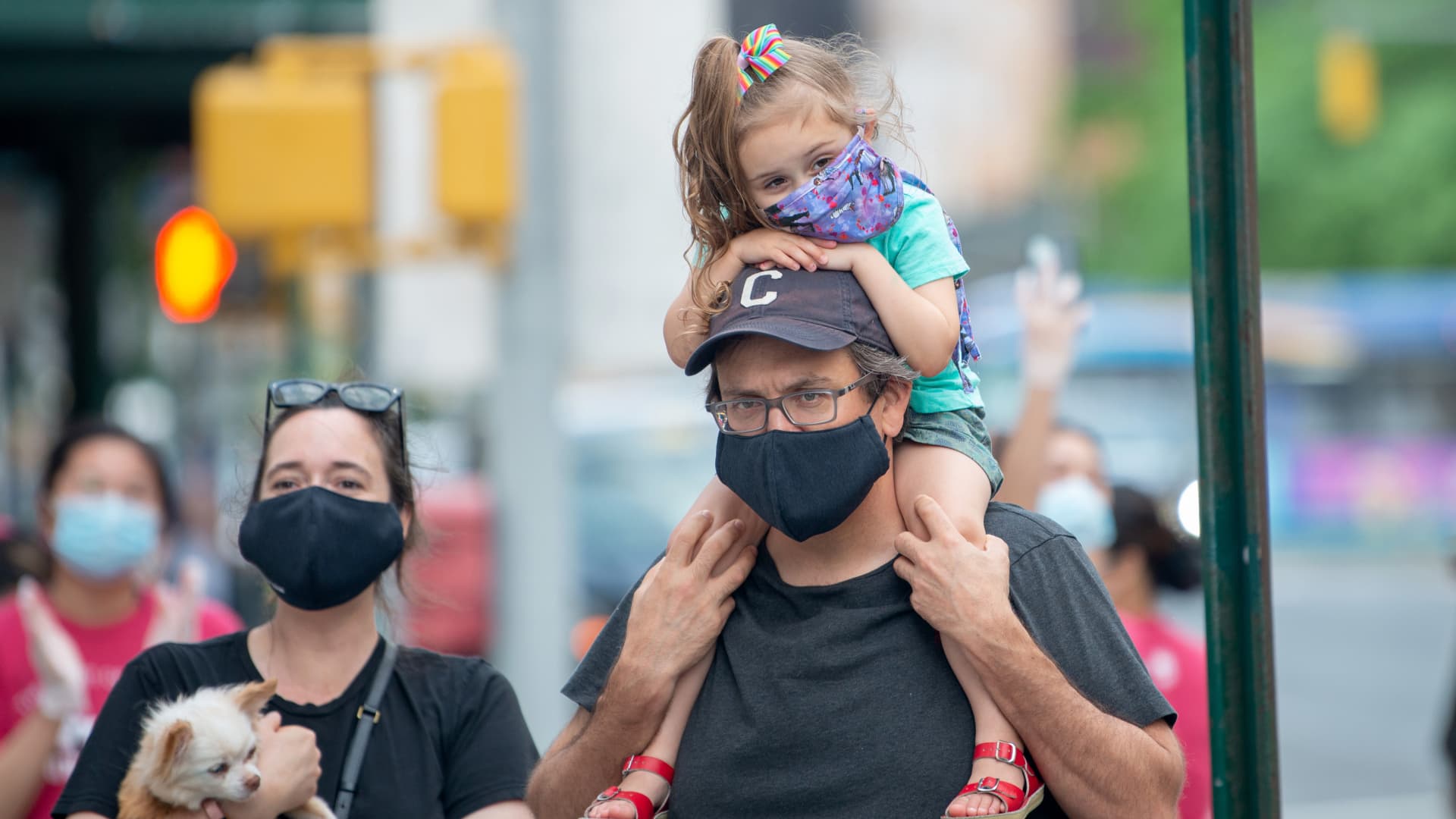 A small child wearing a mask sits on her fathers shoulders outside of the Lenox Health Greenwich Village hospital during the nightly 'Clap Because We Care' cheer for medical staff and essential workers on May 29, 2020 in New York City.