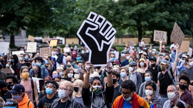 A protester wearing a mask holds a large black power raised fist in the middle of the crowd that gathered at Columbus Circle.