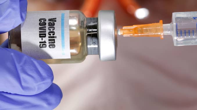 A woman holds a small bottle labeled with a "Vaccine COVID-19" sticker and a medical syringe in this illustration taken April 10, 2020.