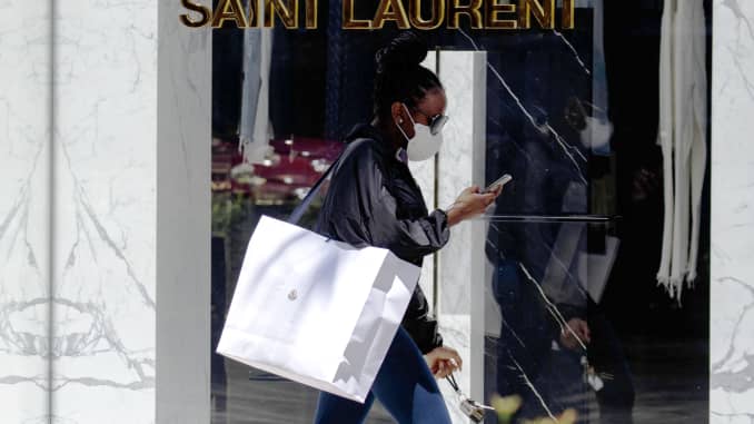 A customer wearing a protective mask carries a Moncler SpA shopping bag past an Yves Saint Laurent store on Rodeo Drive in Beverly Hills, California, U.S., on Tuesday, May 19, 2020.