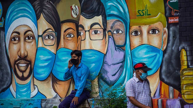 Pedestrians wearing protective face masks in front of a mural in New Delhi, India on July 21, 2020.