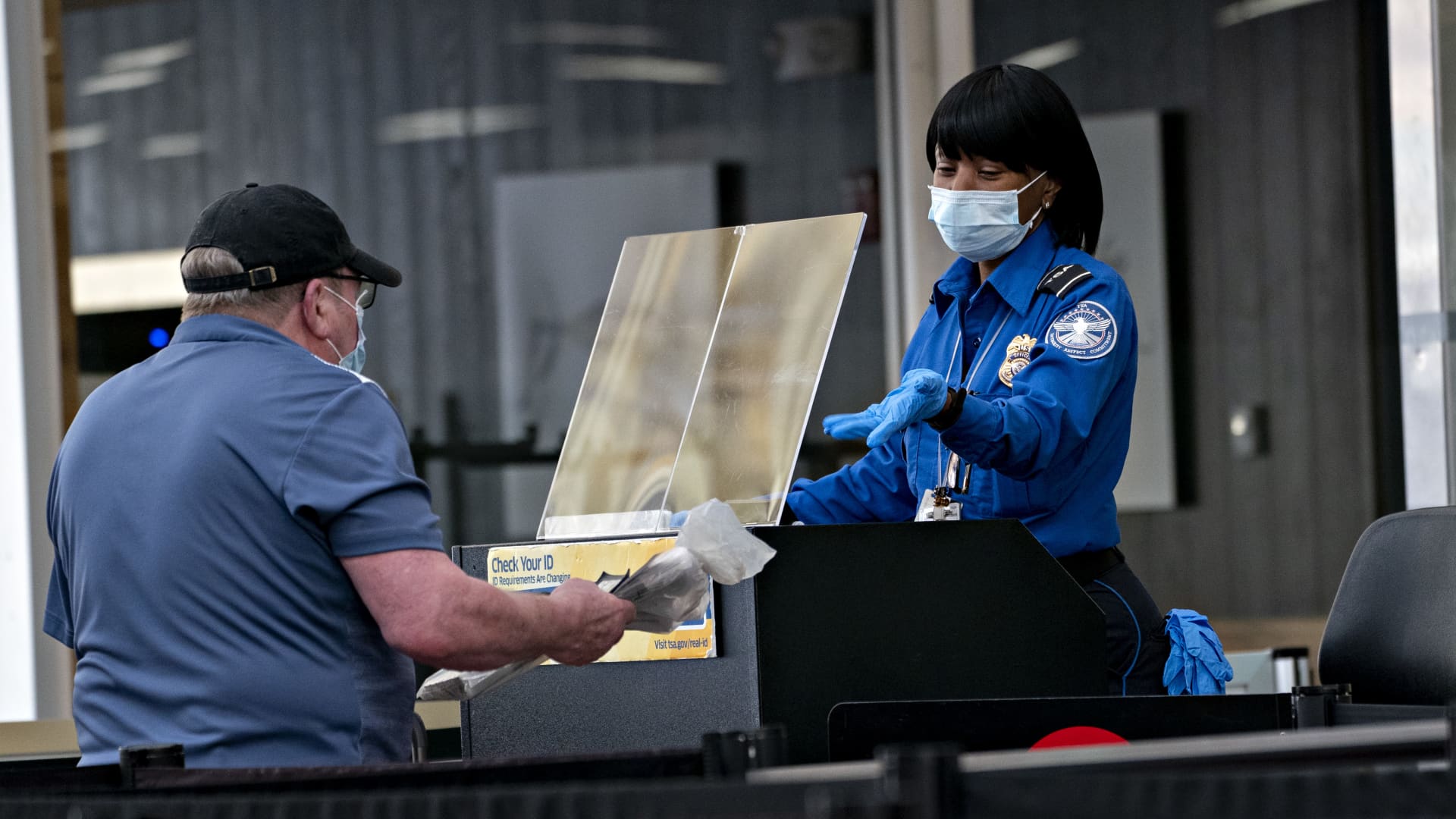 A Transportation Security Administration (TSA) agent wears a protective mask and stands behind a protective barrier while screening a traveler at Ronald Reagan National Airport (DCA) in Arlington, Virginia, U.S., on Tuesday, June 9, 2020.