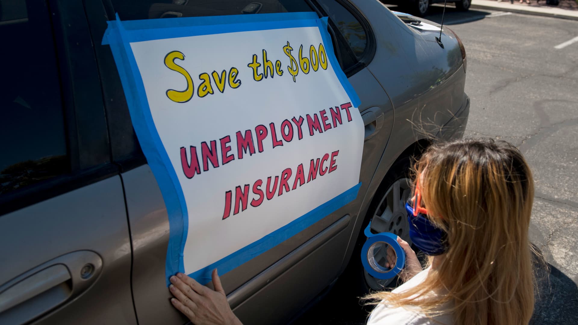 A participant tapes a sign to her car before an Aug. 6, 2020, caravan rally on the Las Vegas Strip in support of extending $600 unemployment benefit.