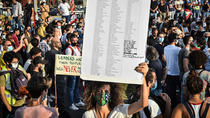 Một phụ nữ cầm biểu ngữ ghi tên các nạn nhân của Vụ nổ Beirut trong cuộc biểu tình gần cảng, vào ngày 11 tháng 8 năm 2020 tại Beirut, Lebanon. Vụ nổ tuần trước khiến hơn 200 người thiệt mạng và hàng nghìn người khác bị thương, được nhiều người Lebanon coi là biểu hiện chết người của sự sơ suất của chính phủ.