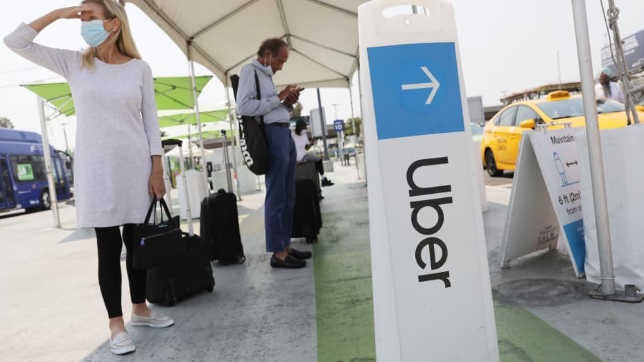 Air travelers wait in the ride share lot near a sign for Uber at Los Angeles International Airport (LAX) on August 20, 2020 in Los Angeles, California.