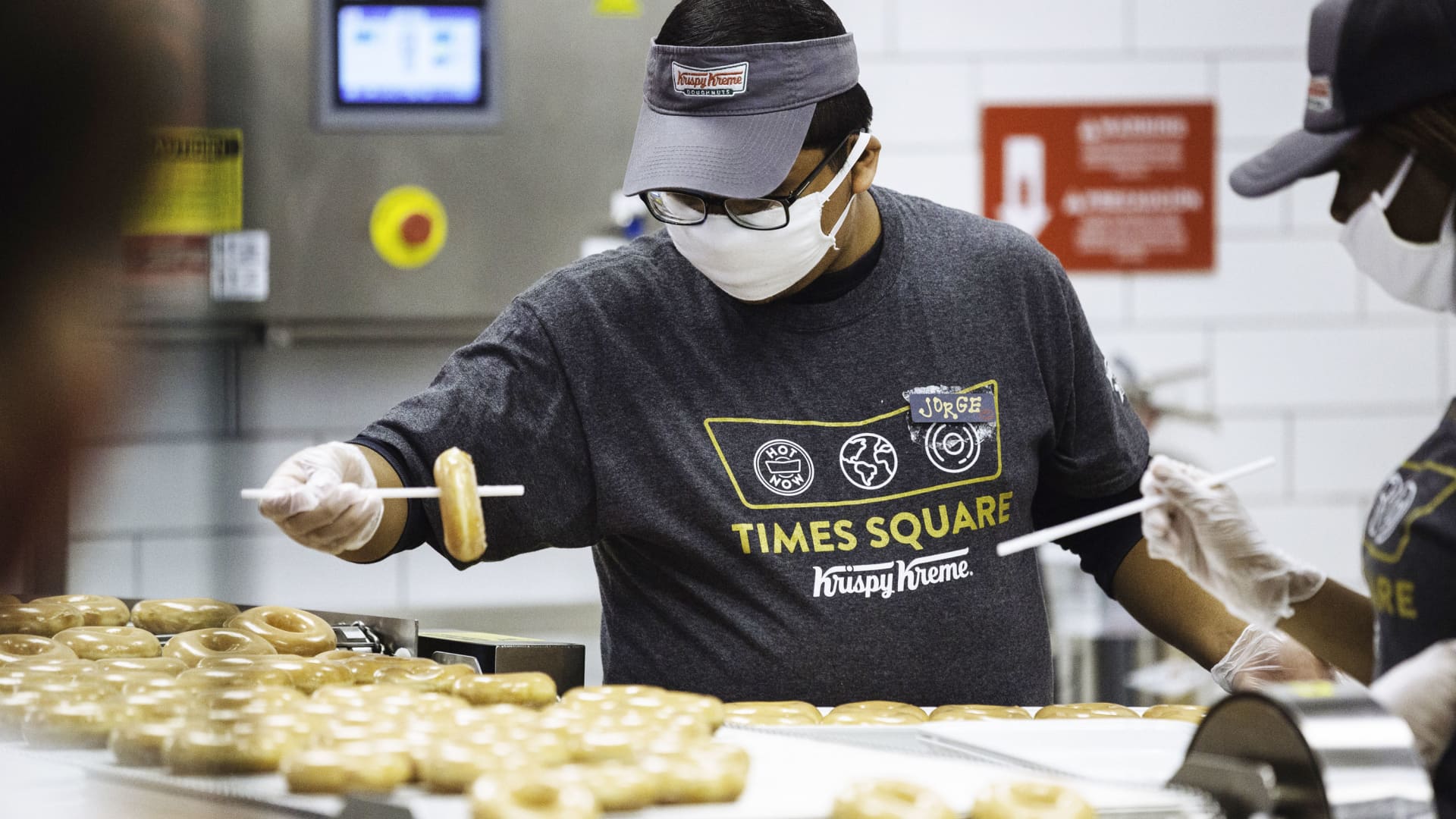 An employee wearing a protective mask removes a doughnut from a production line inside a Krispy Kreme Doughnuts Inc. store in the Times Square neighborhood of New York, on Thursday, Sept. 10, 2020.