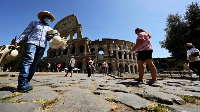 Un vendedor callejero con una máscara facial (L) propone sombreros de paja a los turistas fuera del monumento del Coliseo el 22 de agosto de 2020 en Roma durante la infección por Covid-19, causada por el nuevo coronavirus.