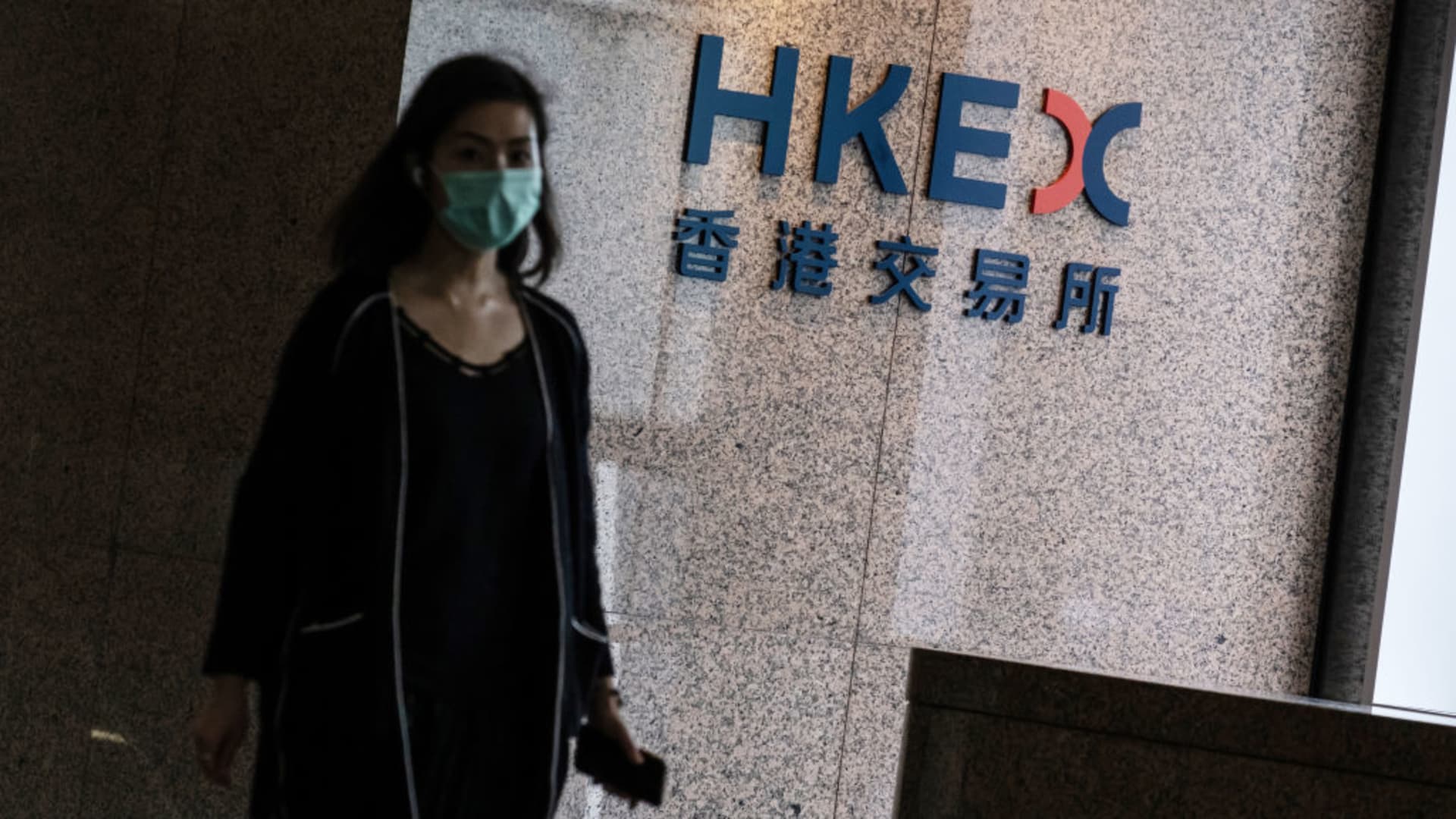 A person wearing a protective mask walks past signage for Hong Kong Exchanges & Clearing Ltd. (HKEX) displayed at the Exchange Square complex in Hong Kong, China, on Wednesday, Aug. 19, 2020.