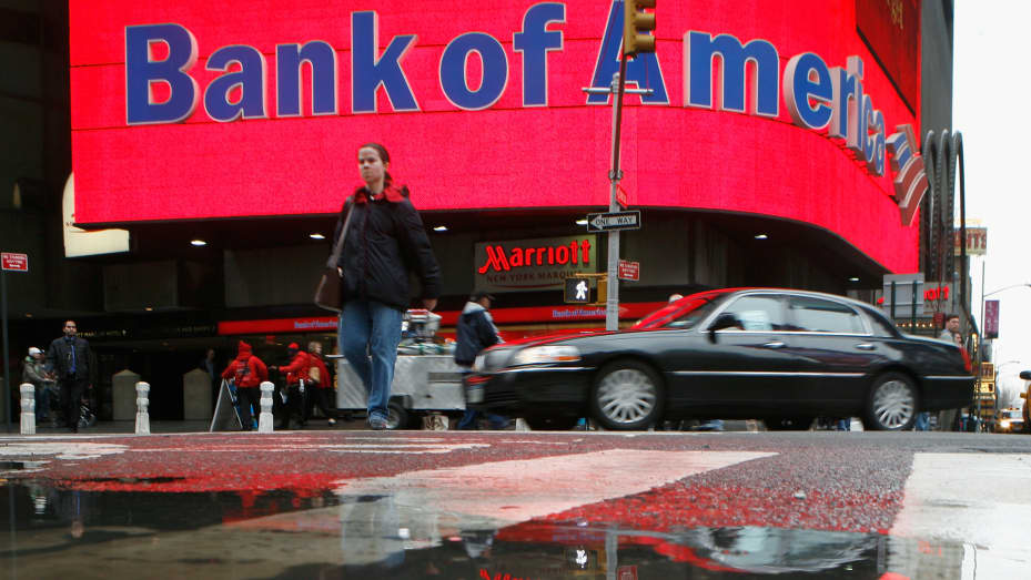 A woman is reflected in a puddle as she passes a Bank of America branch in New York's Times Square.
