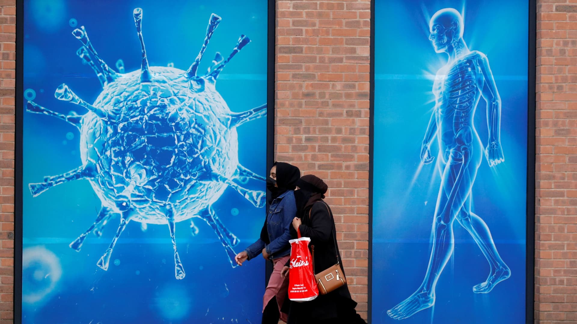 People walk past an illustration of a virus outside a regional science centre, as the city and surrounding areas face local restrictions in an effort to avoid a local lockdown being forced upon the region, amid the coronavirus disease (COVID-19) outbreak, in Oldham, Britain August 3, 2020.
