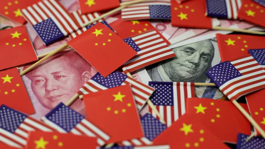 Un billete de dólar estadounidense con el padre fundador de Estados Unidos, Benjamin Franklin, y un billete de yuan chino con el difunto presidente chino, Mao Zedong, se ven entre las banderas de Estados Unidos y China.