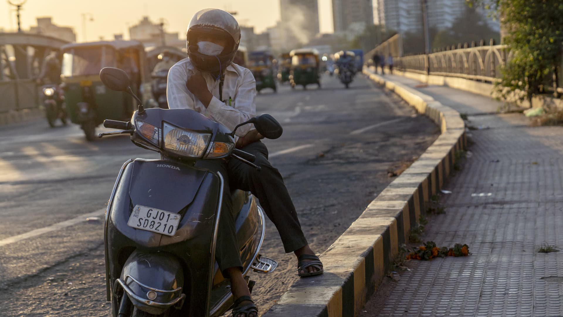 A motorcyclist wears a protective mask while sitting at the side of the road at the Sabarmati Riverfront in Ahmedabad, India, on Thursday, Oct. 22, 2020. Prime Minister Narendra Modi said his government will ensure that all 1.3 billion people nationwide will have access to a Covid-19 vaccine as soon it is ready.