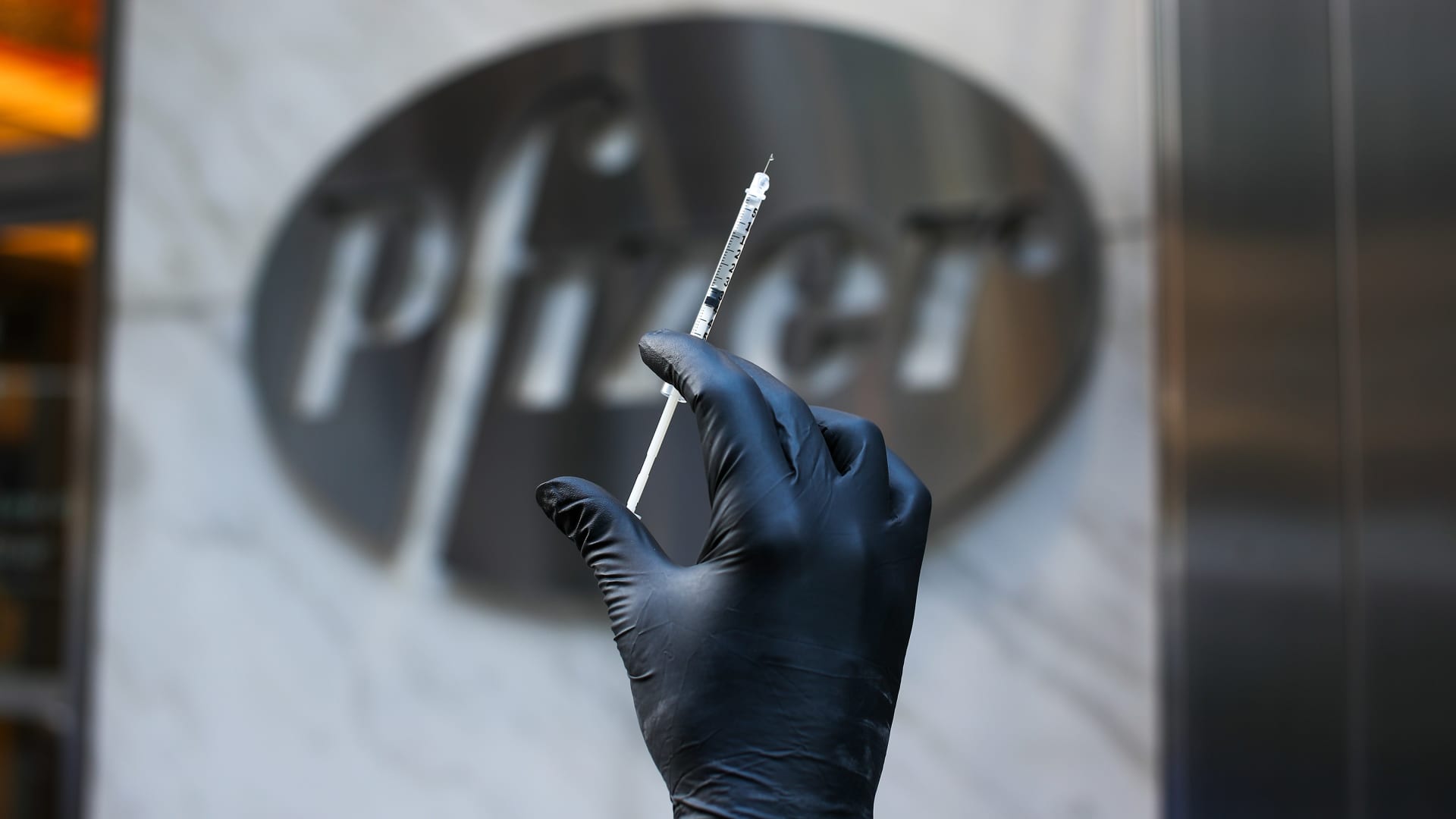 A syringe is seen by the logo of Pfizer's headquarter in Manhattan, New York City, United States on November 19, 2020.