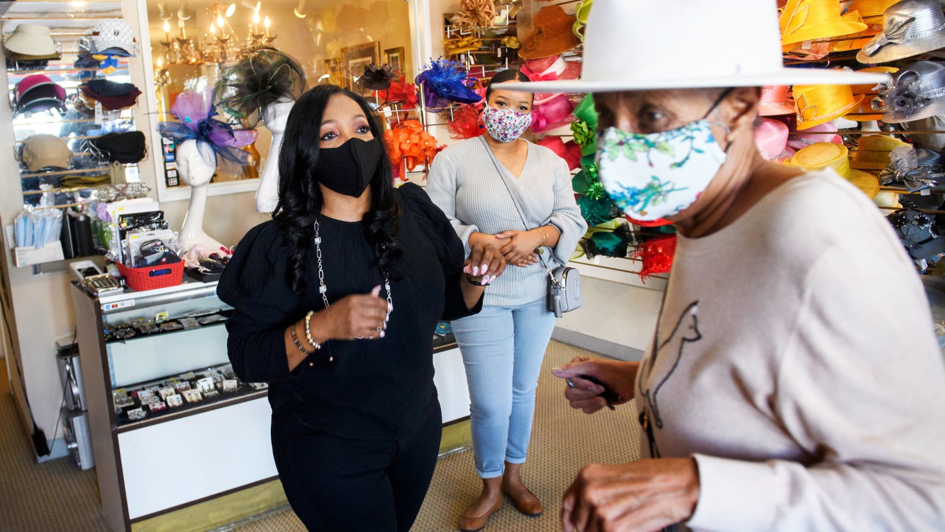 Customer Tamara Jenkins tries on a hat with Meeka Robinson Davis, owner of One-Of-A-Kind Hats, as Davis' daughter Chrstiana Davis looks on, at the store in the Windsor Hills neighborhood of Los Angeles, California, November 24, 2020.