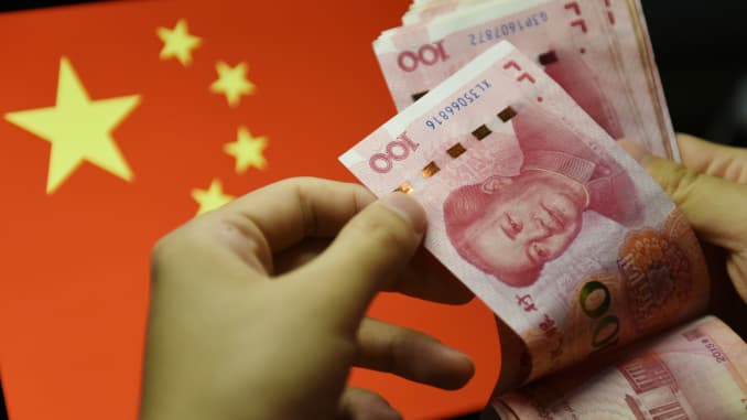 Un hombre cuenta billetes de 100 RMB con la bandera china de fondo.