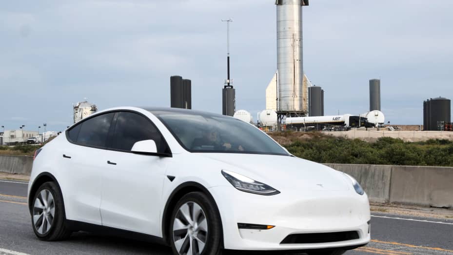 A man drives his Tesla car as the Starship SN8 of SpaceX is seen behind, days before a test launch of the company's new super heavy-lift Starship rocket from their facilities in this small town of Boca Chita, Texas, December 4, 2020.