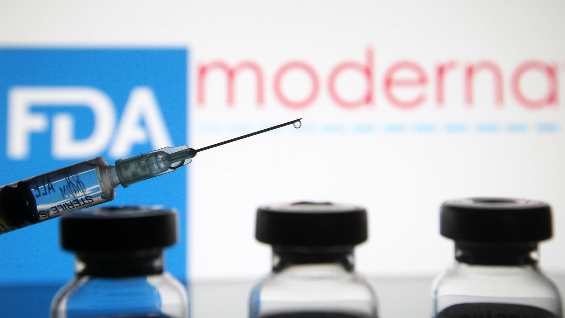 Vials and a medical syringe seen displayed in front of the Food and Drug Administration (FDA) of the United States and Moderna biotechnology company's logos. FDA finds the COVID-19 vaccine.