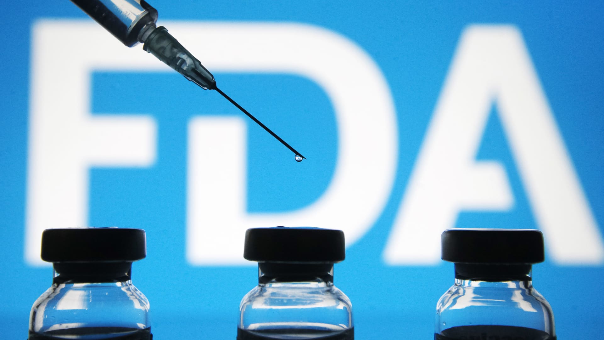 Vials and a medical syringe seen displayed in front of the Food and Drug Administration (FDA) of the United States logo. FDA finds the COVID-19 vaccine.