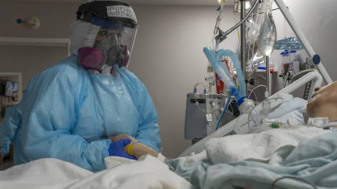 La miembro del personal médico Christina Mathers atiende a un paciente, que está inconsciente, mientras sostiene la mano del paciente en la unidad de cuidados intensivos (UCI) COVID-19 en el United Memorial Medical Center el 21 de diciembre de 2020 en Houston, Texas.