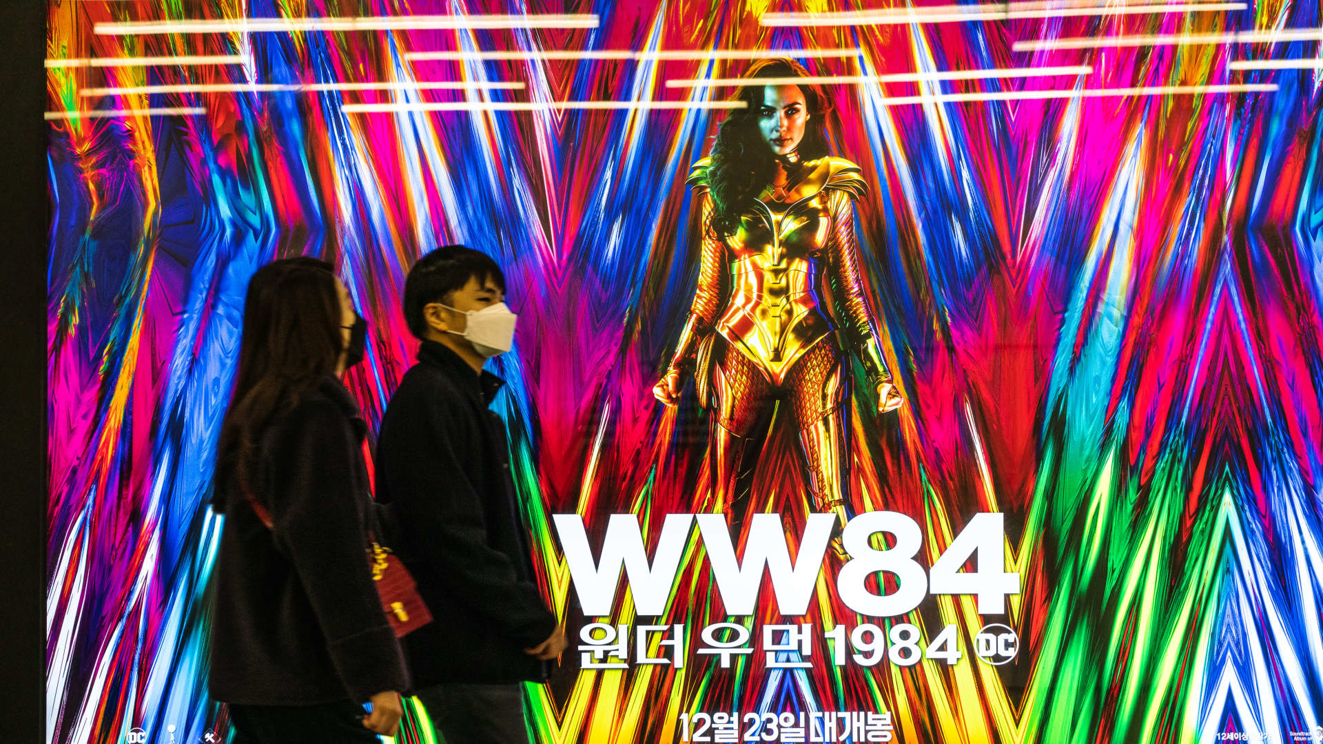 People wearing masks walk past an advertising billboard of the movie 'Wonder Woman 1984'. Photo taken on 26 Dec. 2020.
