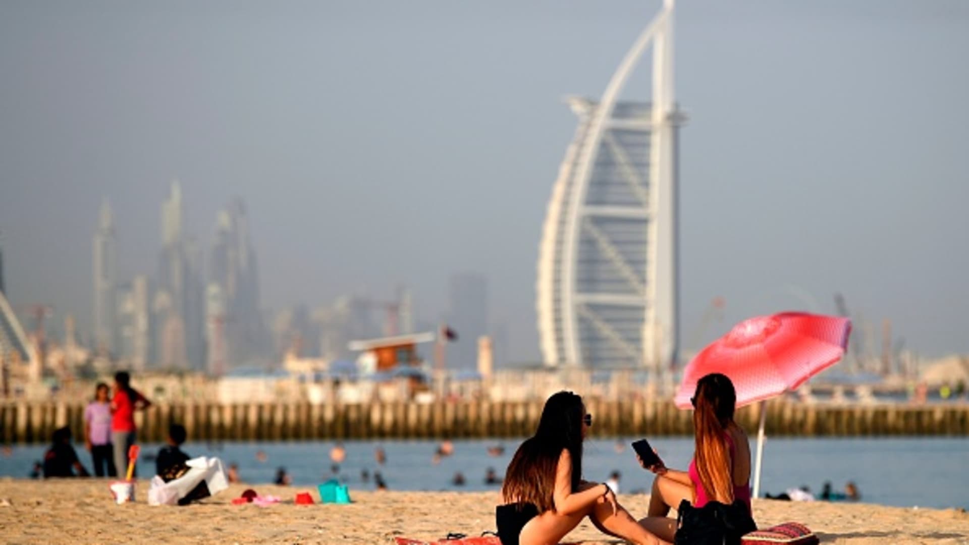 Woman sunbathers sit along a beach in the Gulf emirate of Dubai on July 24, 2020, while behind is seen the Burj al-Arab hotel.