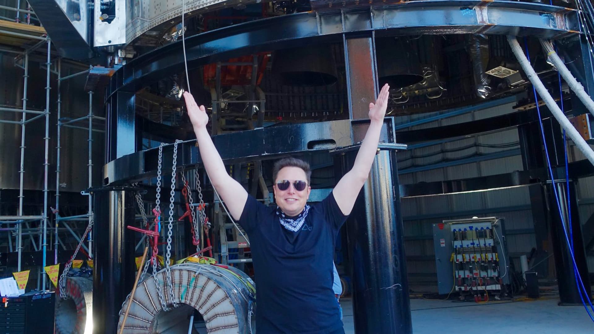 SpaceX CEO Elon Musk raises his arms in celebration beneath a Starship rocket prototype under construction in Boca Chica, Texas.