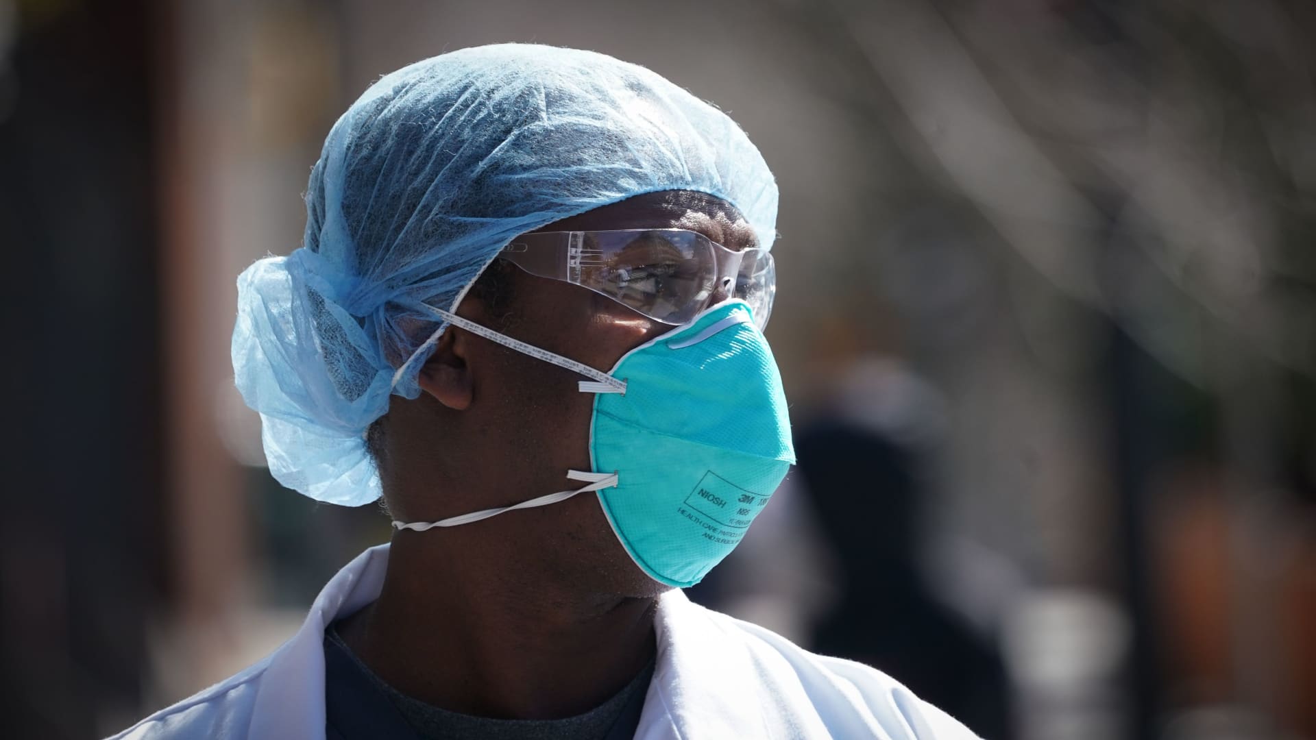 A healthcare worker wears a N95 respirator with two straps that fit around the head.