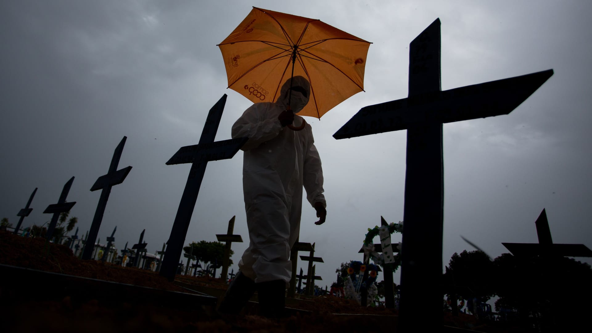 A worker wearing a protective suit and carrying an umbrella walks past the graves of COVID-19 victims at the Nossa Senhora Aparecida cemetery, in Manaus, Brazil, on February 25, 2021.