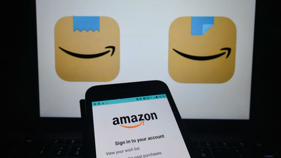 An illustrative image of Amazon Shopping app seen on a mobile phone screen in front of an old (L) and a new (R) Amazon Shopping app icons displayed on a screen. Amazon has quietly changed its new Amazon Shopping app icon, replacing the blue ribbon on top