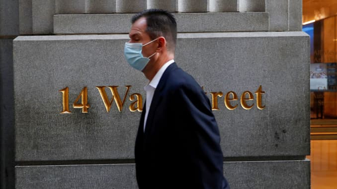 A man wearing a protective face mask walks by 14 Wall Street in the financial district of New York, November 19, 2020.