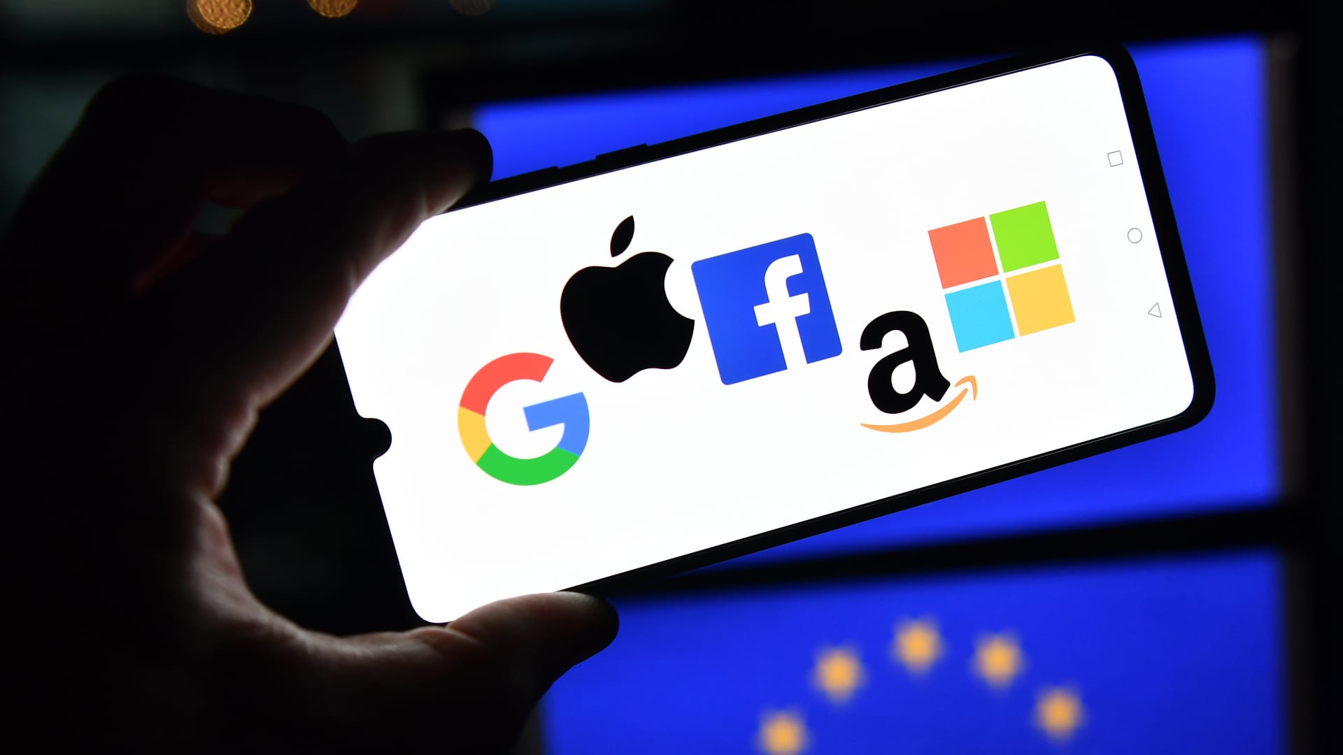 The logos of Google, Apple, Facebook, Amazon and Microsoft displayed on a mobile phone with an EU flag pictured in the background.