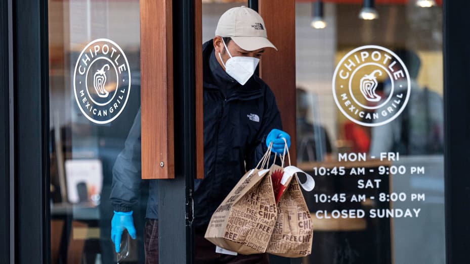 A person wearing a protective mask and gloves exits a Chipotle restaurant in San Francisco, California, U.S., on Monday, April 19, 2021.