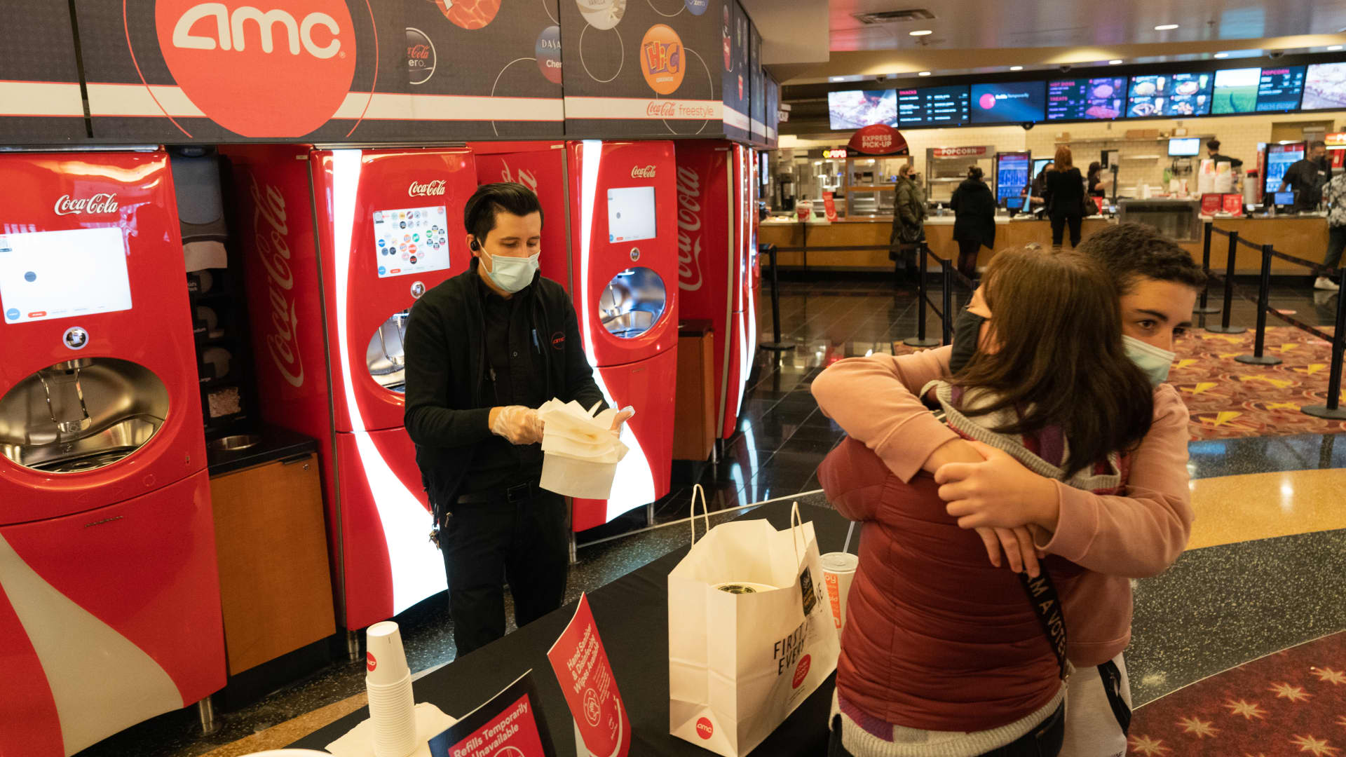 A son hugs his mother as a concessions worker hands over napkins and soda inside the AMC movie theater at the Westfield Century City shopping mall in Los Angeles, California, on Monday, March 15, 2021.