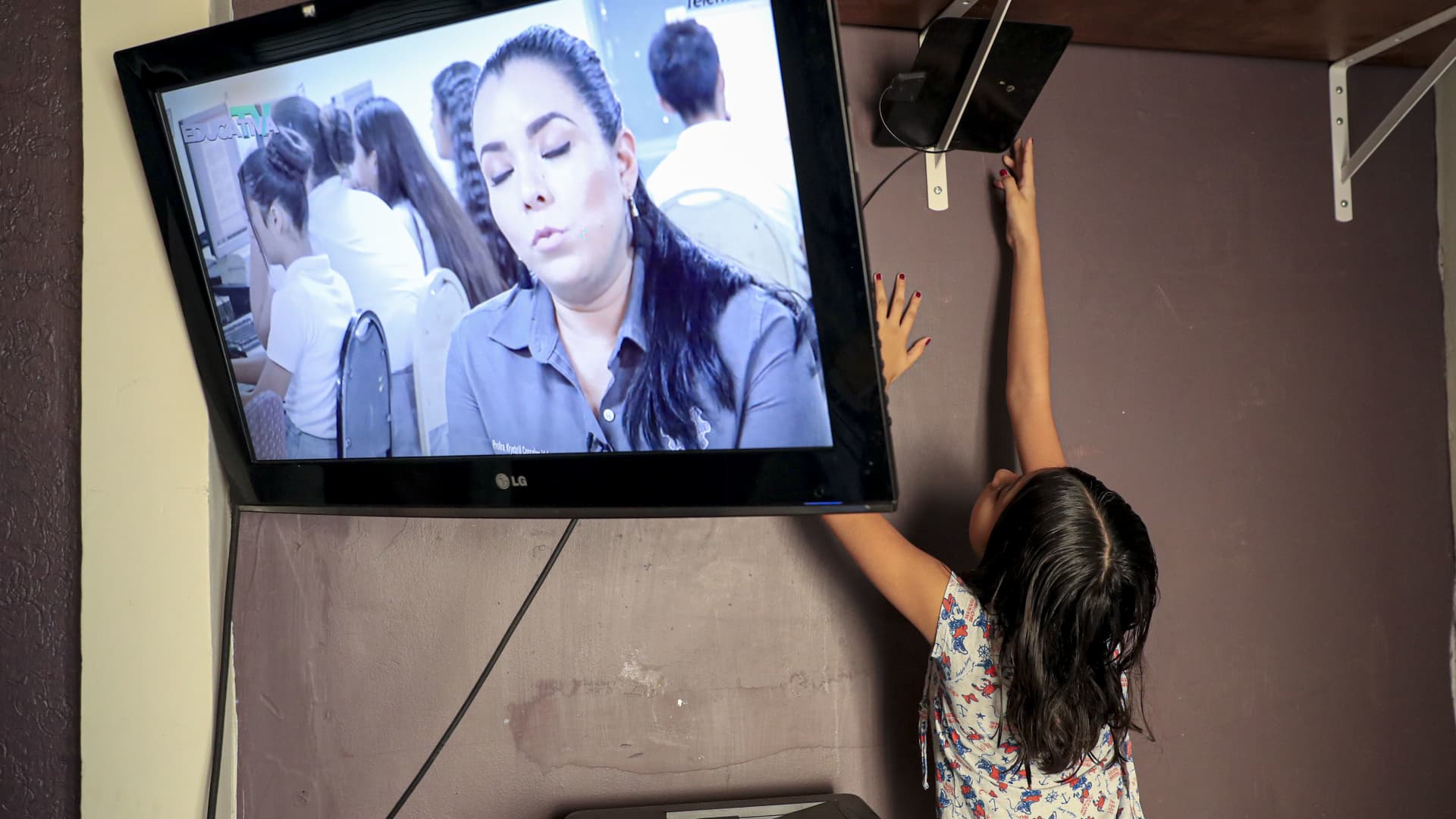 A young girl adjusts the antenna of a television in an attempt to obtain a digital signal.