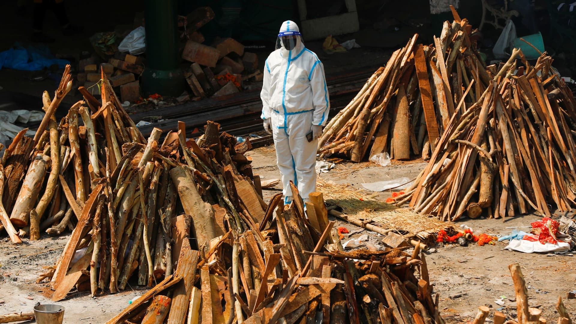 A man wearing personal protective equipment (PPE) stands next to funeral pyres of those who died from the coronavirus disease (COVID-19), during a mass cremation, at a crematorium in New Delhi, India April 26, 2021.