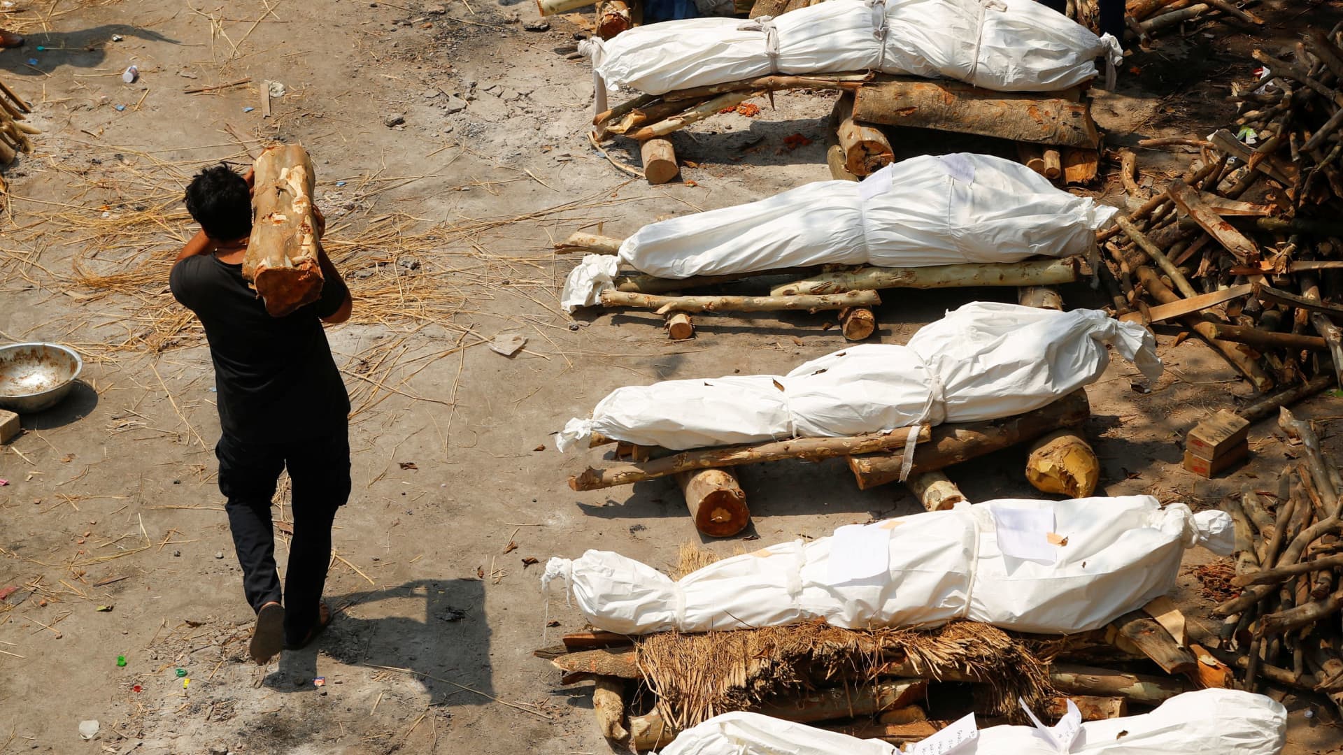 A man carrying wood walks past the funeral pyres of those who died from the coronavirus disease (COVID-19), during a mass cremation, at a crematorium in New Delhi, India April 26, 2021.