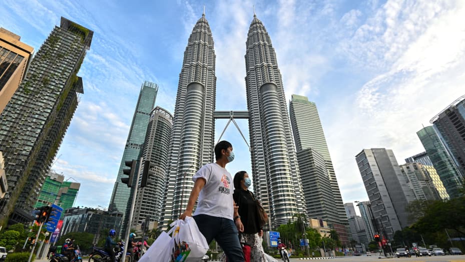 People wearing face masks walk in front of the Petronas Twin Towers in Kuala Lumpur, Malaysia, Jan. 29, 2021.