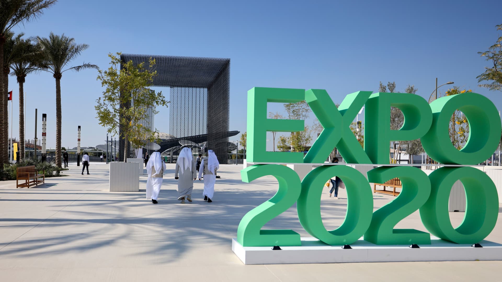 People walk past the official sign marking the Dubai Expo 2020 near the Sustainability Pavilion in Dubai on January 16, 2021. - The six-month world fair, a milestone for the emirate which has splashed out $8.2 billion on the eye-popping venue in the hope of boosting its soft power and resetting the economy, will now open its doors in October 2021.