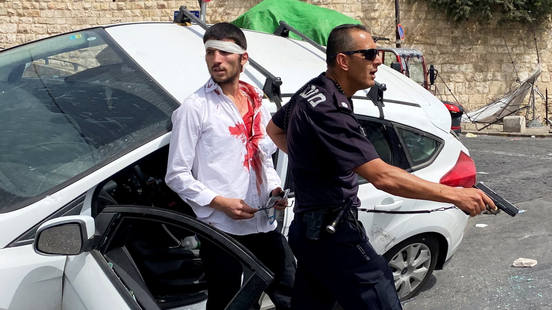 An Israeli police officer holds his weapon as he stands in front of an injured Israeli driver moments after witnesses said his car crashed into a Palestinian on a pavement during stone-throwing clashes near Lion's Gate just outside Jerusalem's Old City May 10, 2021.