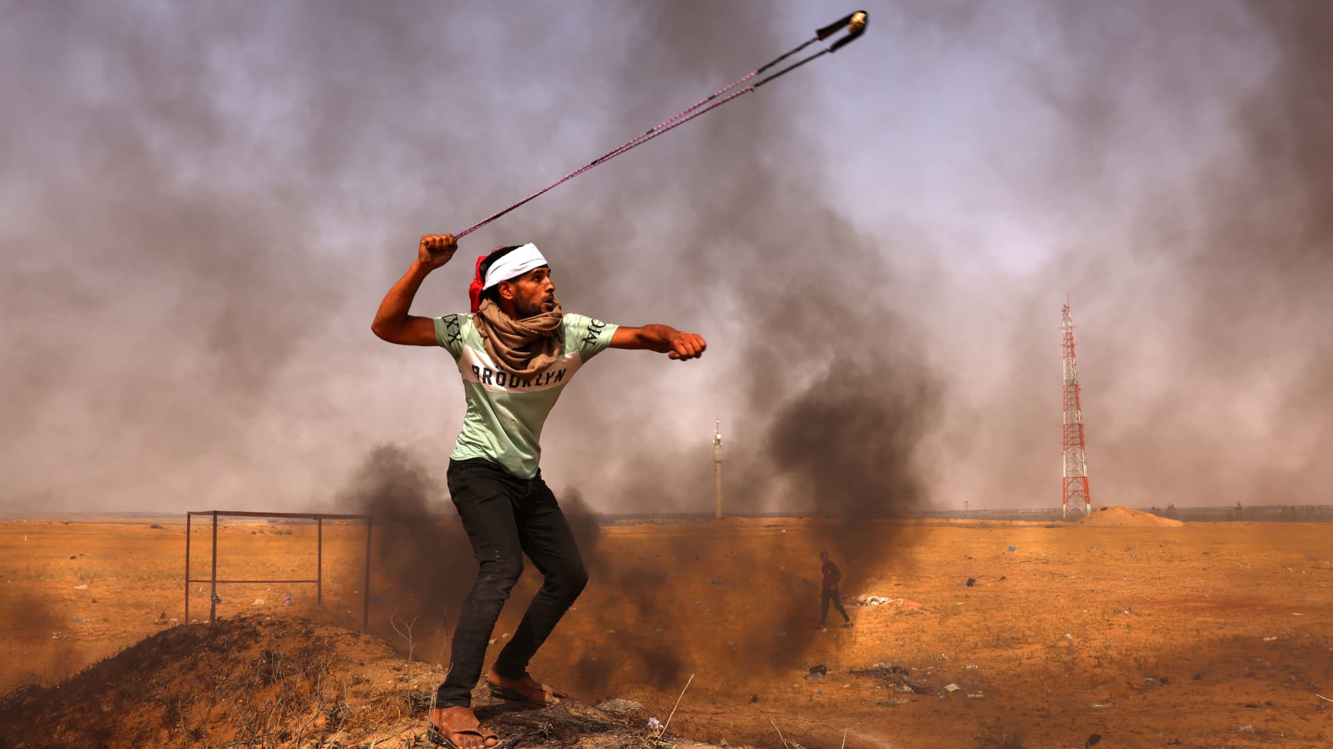 A Palestinian demonstrator hurls rocks with a slingshot next to burning tires during a protest by the border with Israel, east of Rafah in the southern Gaza Strip, on May 10, 2021.