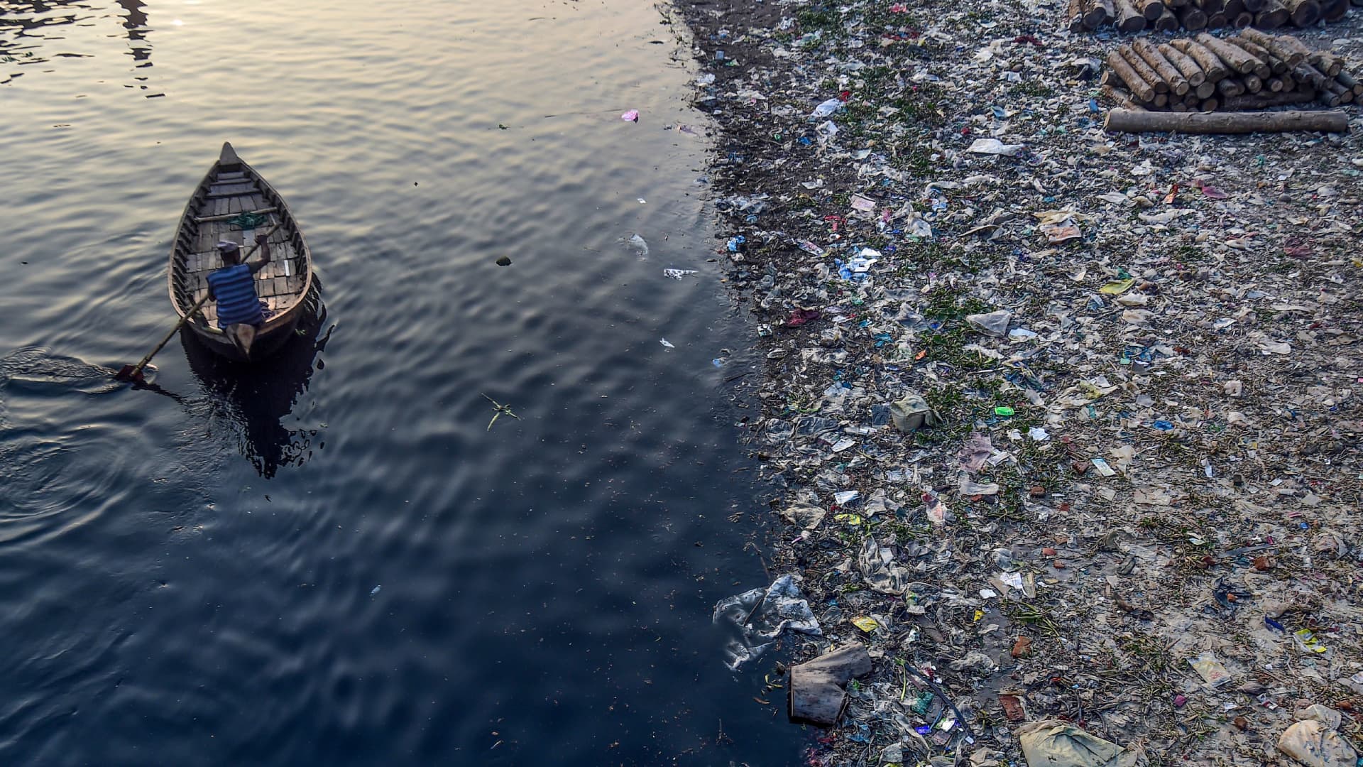 A man paddles on a boat as plastic bags float on the water surface of the Buriganga river in Dhaka on January 21, 2020.