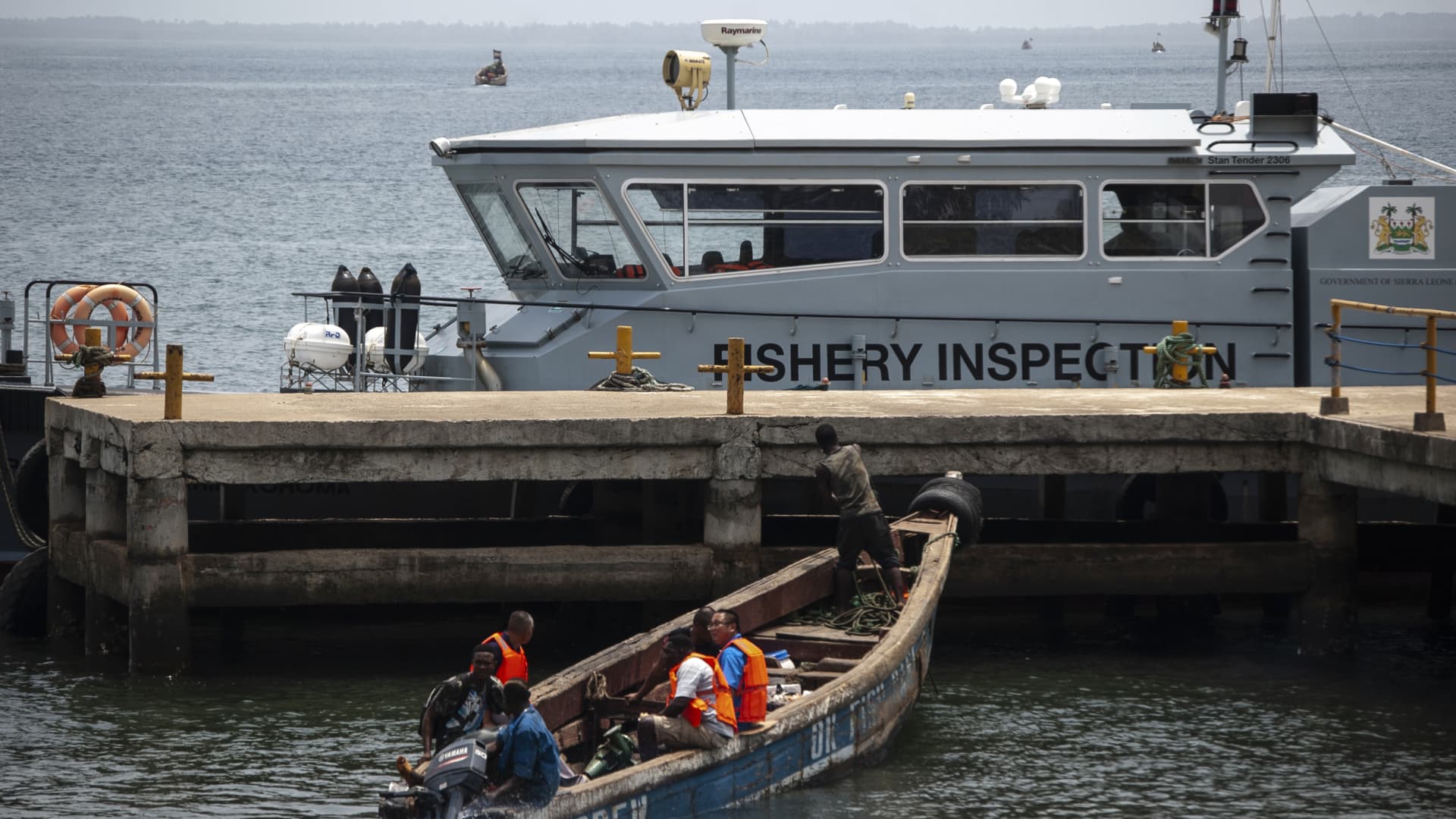 Chinese fishermen in a wooden carved boat are seen at the port in Freetown's Murray Town suburb on April 8, 2019 with the only Joint Maritime Committee (JMC) offshore patrol boat, donated by the World Bank, in the background.