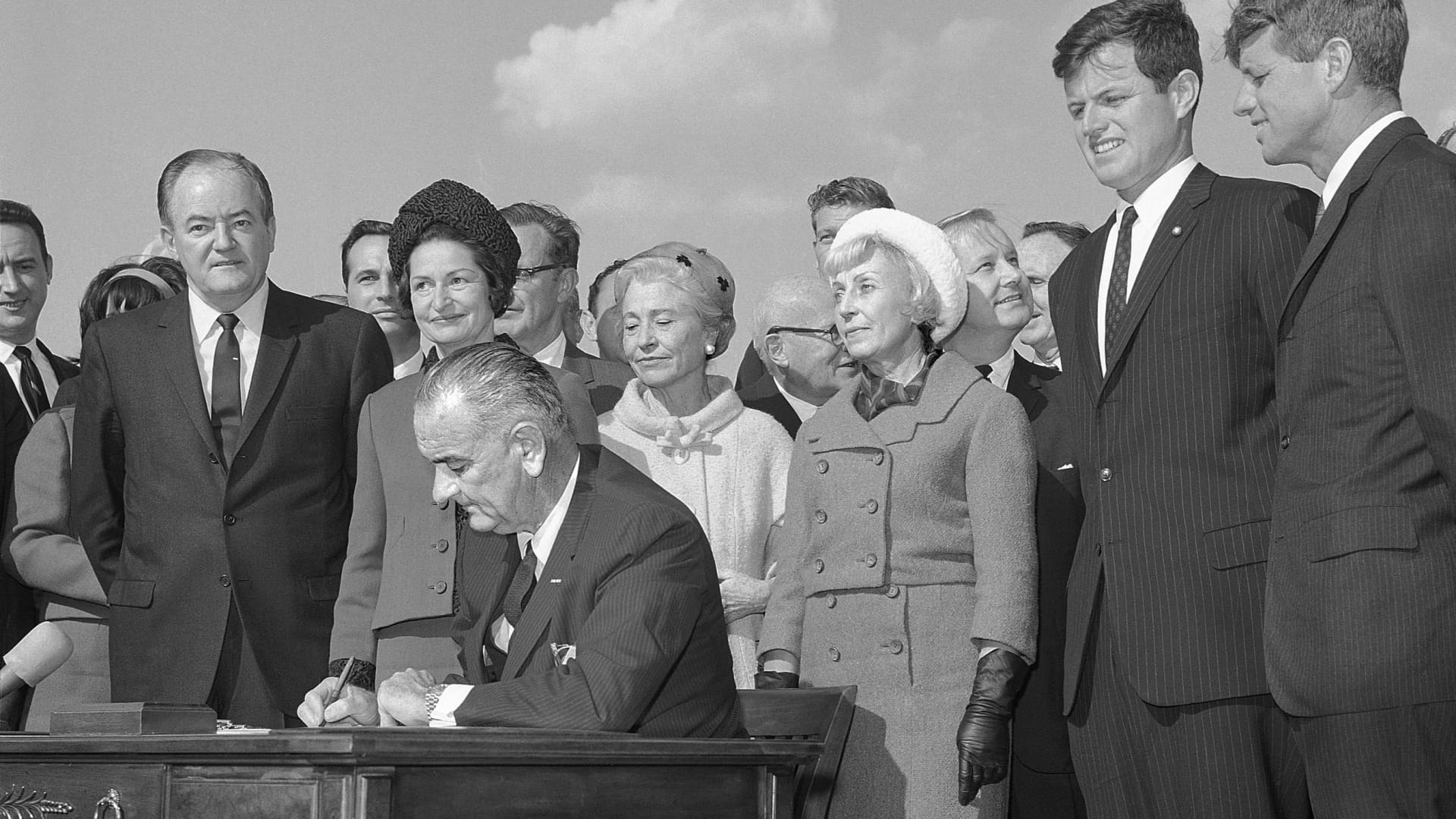 President Lyndon Johnson signs the liberalized U.S. Immigration bill into law. Attending the ceremony on Liberty Island, (L-R) are: Vice President Hubert Humphrey; first lady Lady Bird Johnson; Mrs. Mike Mansfield (wife of the Senate Majority Leader); Muriel Humphrey; Sen. Ted Kennedy and Sen. Robert Kennedy, on October 4, 1965.