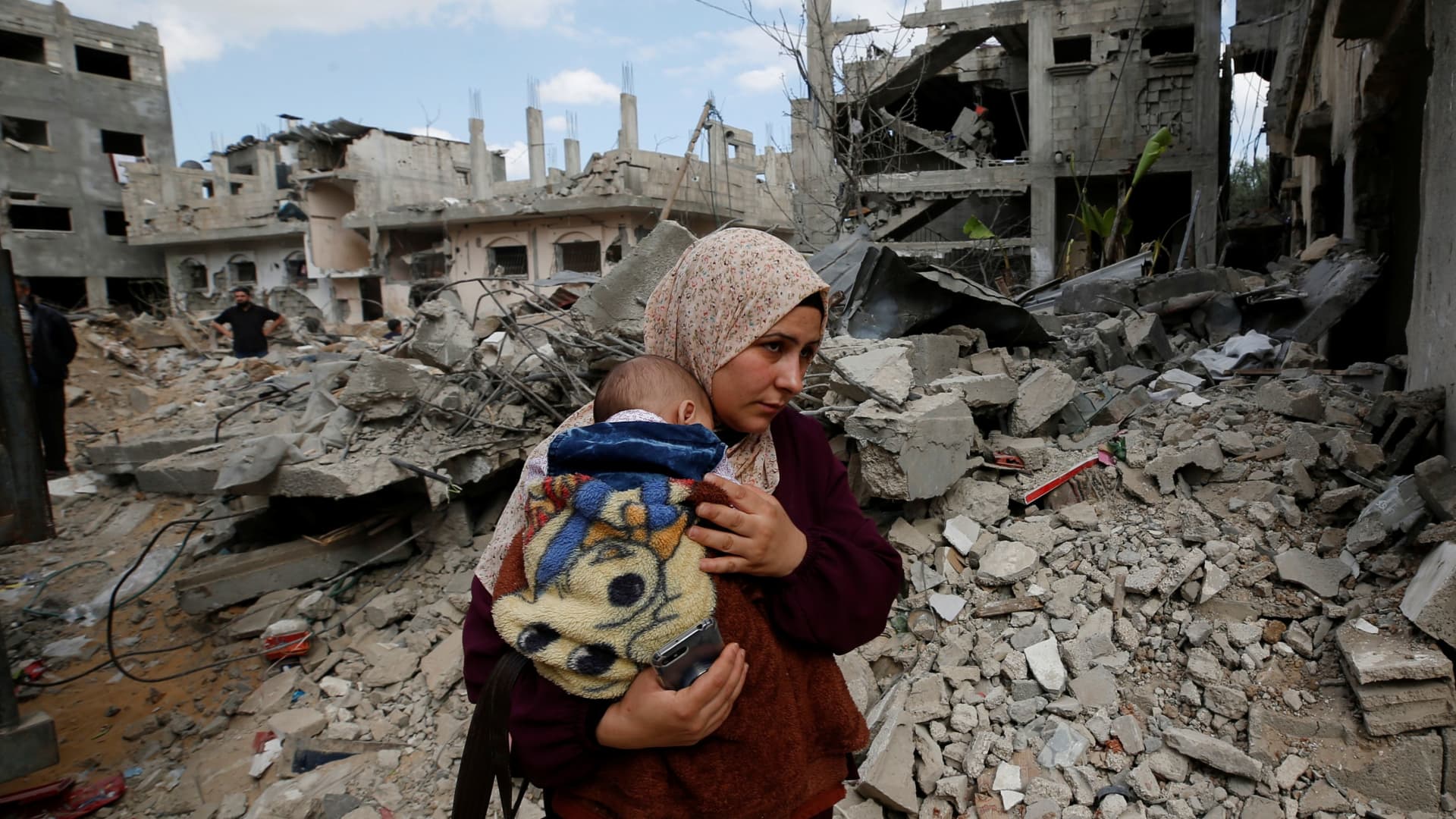 A Palestinian woman carries her child amid the rubble of their houses which were destroyed by Israeli air strikes during the Israel-Hamas fighting in Gaza May 23, 2021.